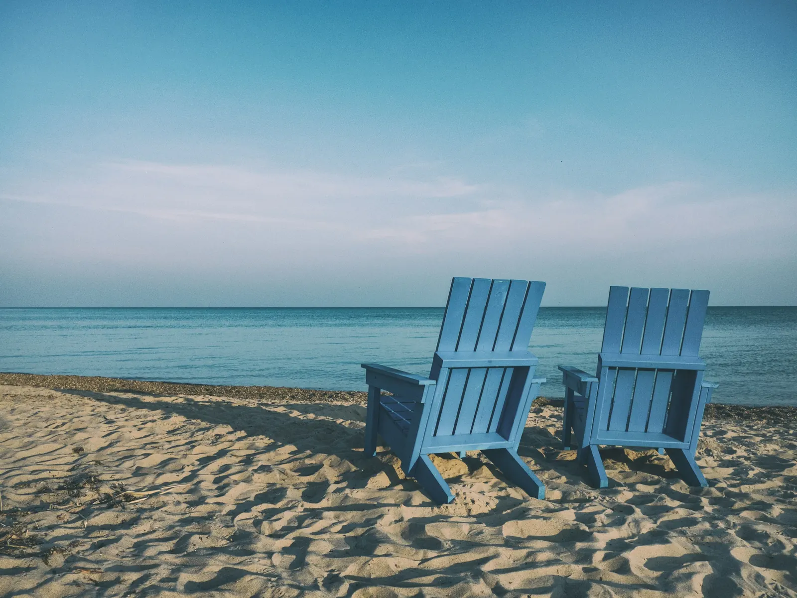 Deux fauteuils bleus face à la mer, sur une plage de sable